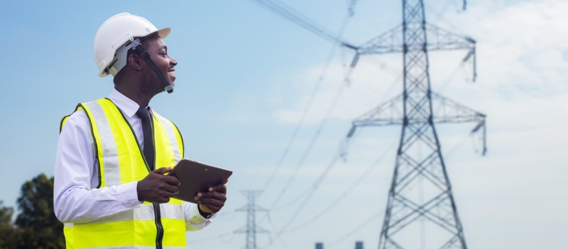 African engineer uses a tablet to operate a high-voltage power system from an electric power plant. Innovative electrical solutions for businesses
