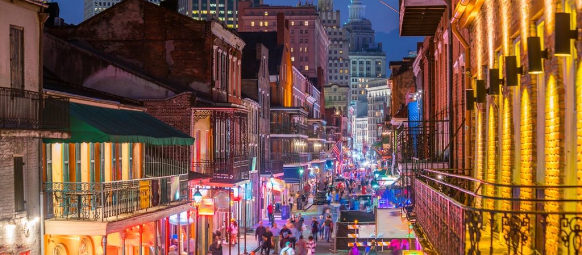Vibrant street view of neon-illuminated pubs and bars in New Orleans' French Quarter, reflecting Mardi Gras festivities.