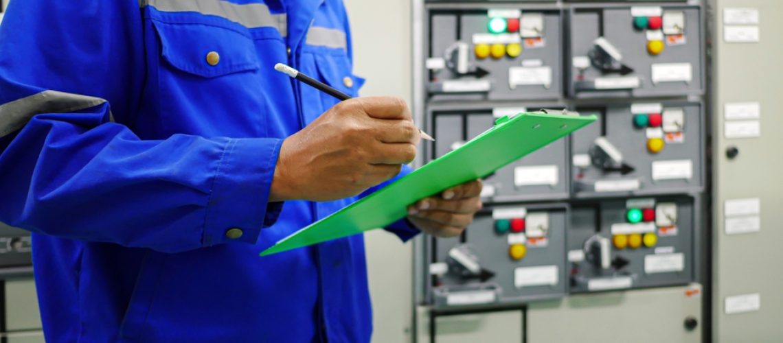Visual inspection of electrical control cabinets at a New Orleans commercial facility, with results recorded on a clipboard.