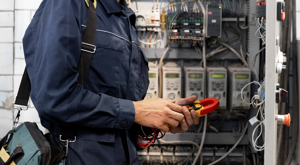 An electrician in New Orleans inspects the electrical circuitry within a control panel to assess high current and voltage levels, initiating and commissioning relays for industrial production.