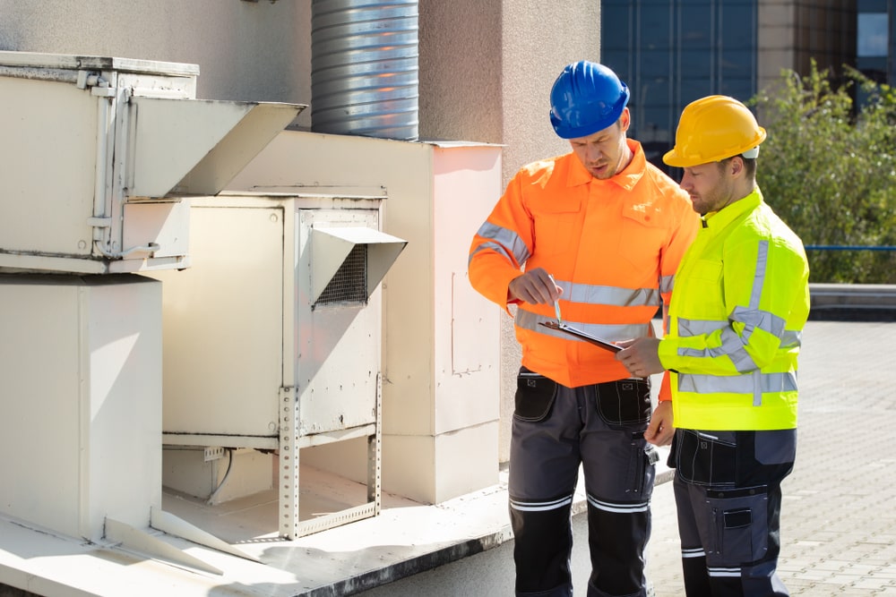 Electricians in safety gear performing electrical testing on a rooftop air conditioning unit, demonstrating commercial electrical maintenance.
