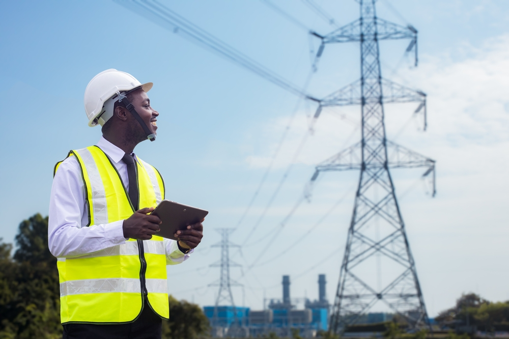African engineer uses a tablet to operate a high-voltage power system from an electric power plant. Innovative electrical solutions for businesses
