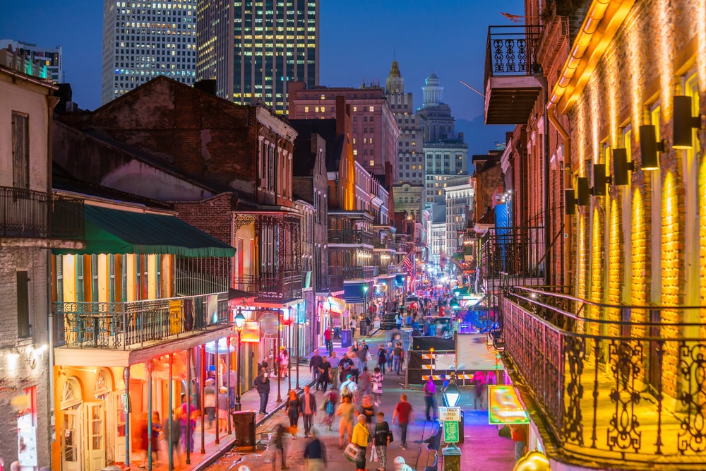 Vibrant street view of neon-illuminated pubs and bars in New Orleans' French Quarter, reflecting Mardi Gras festivities.