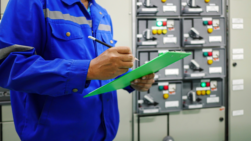 Visual inspection of electrical control cabinets at a New Orleans commercial facility, with results recorded on a clipboard.